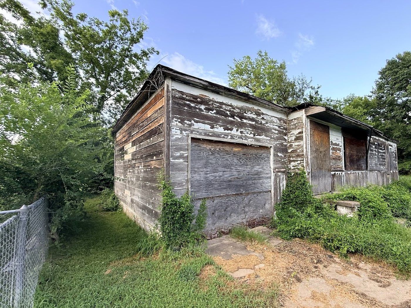 Vacant inherited house in North Tulsa before renovation — weathered boarded-up exterior and overgrown yard